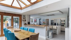 Una cocina moderna con una isla central, un área de comedor con sillas azules y un amplio ventanal con techo de madera.