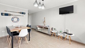 A modern dining area with a wooden table, black chairs, a television mounted on the wall, and a decorative welcome sign.