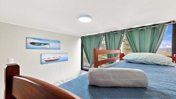Un dormitorio con una cama individual, cabecera de madera, una ventana con cortinas y dos cuadros de barcos colgados en la pared.