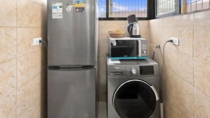 A compact kitchen with a stainless steel refrigerator, a microwave, and a washing machine.