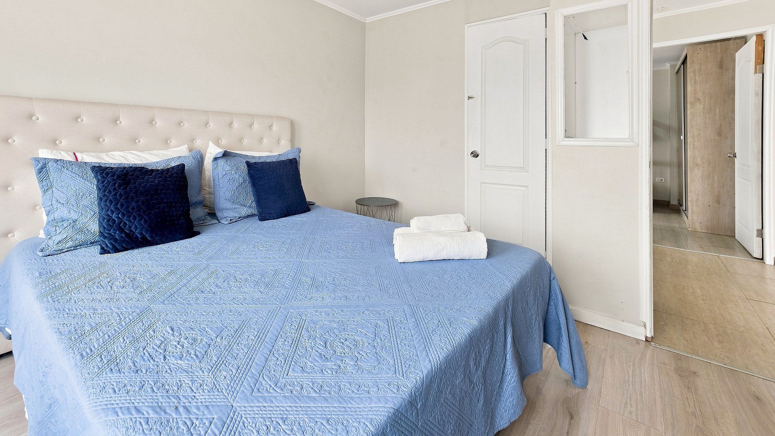 A bedroom with a bed, pillows, a bedside table, and a door leading to another room.