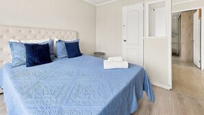 A bedroom with a bed, pillows, a bedside table, and a door leading to another room.