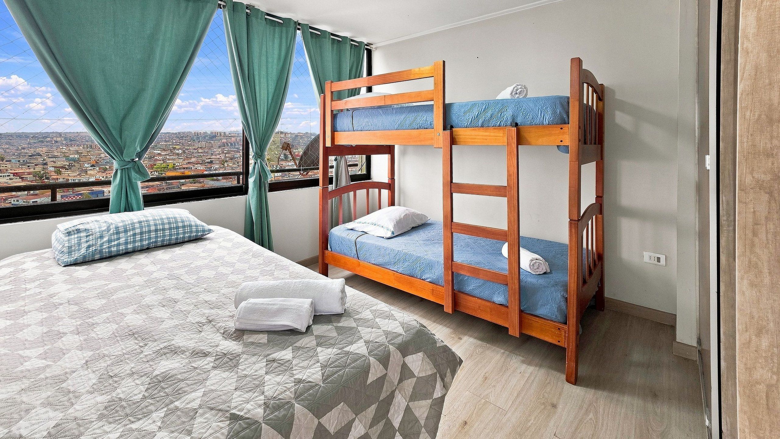 Ein Zimmer mit Etagenbett, Einzelbett und Blick auf die Stadt durch ein Fenster.