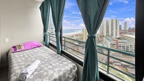 Habitación de hotel con cama, ventana con cortinas y vistas a un paisaje urbano.