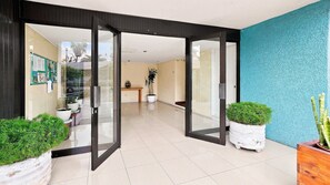 A hotel lobby with a glass door entrance, a reception desk, and potted plants.