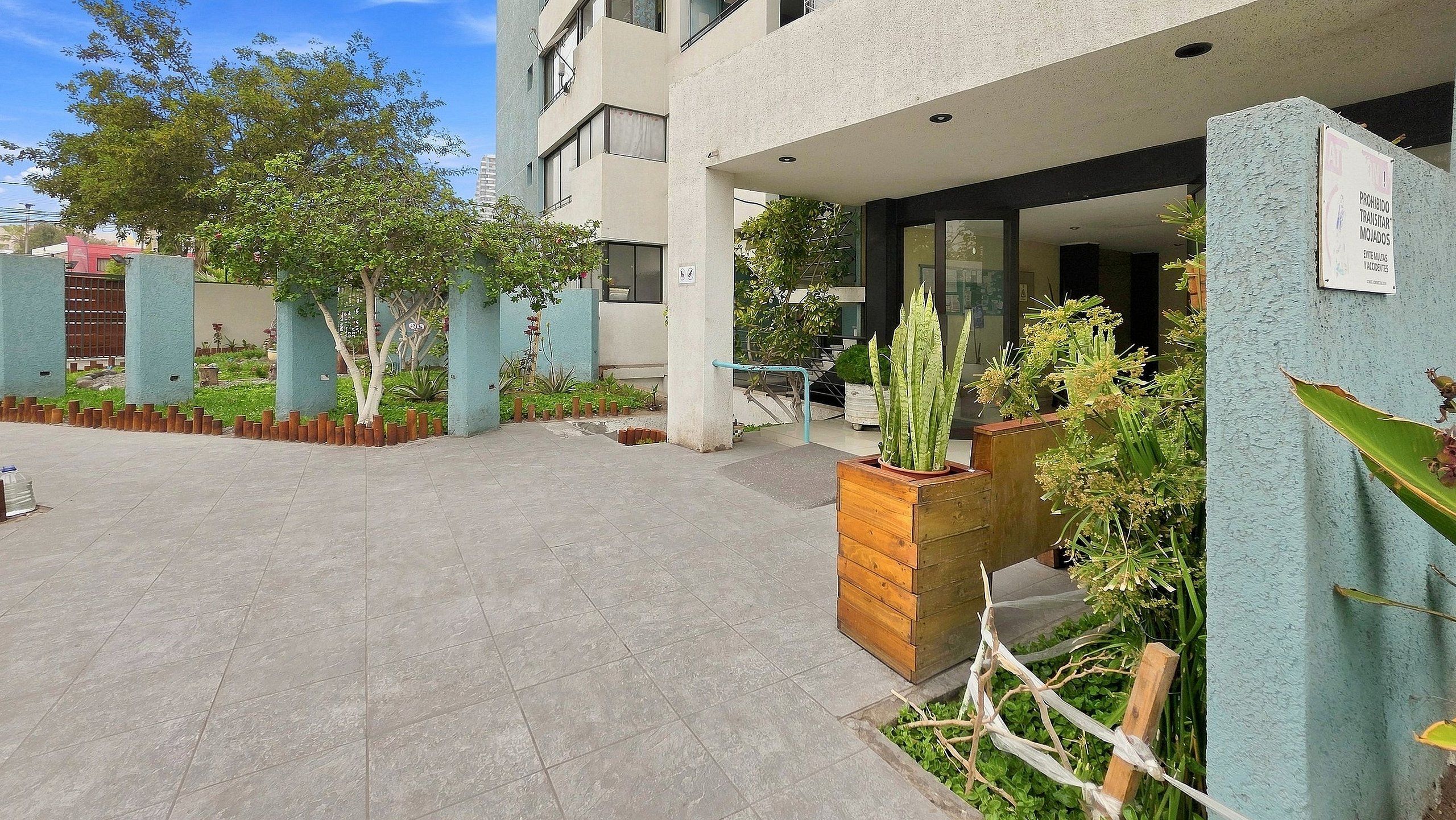 A modern building entrance with a paved courtyard, potted plants, and a sign prohibiting parking.