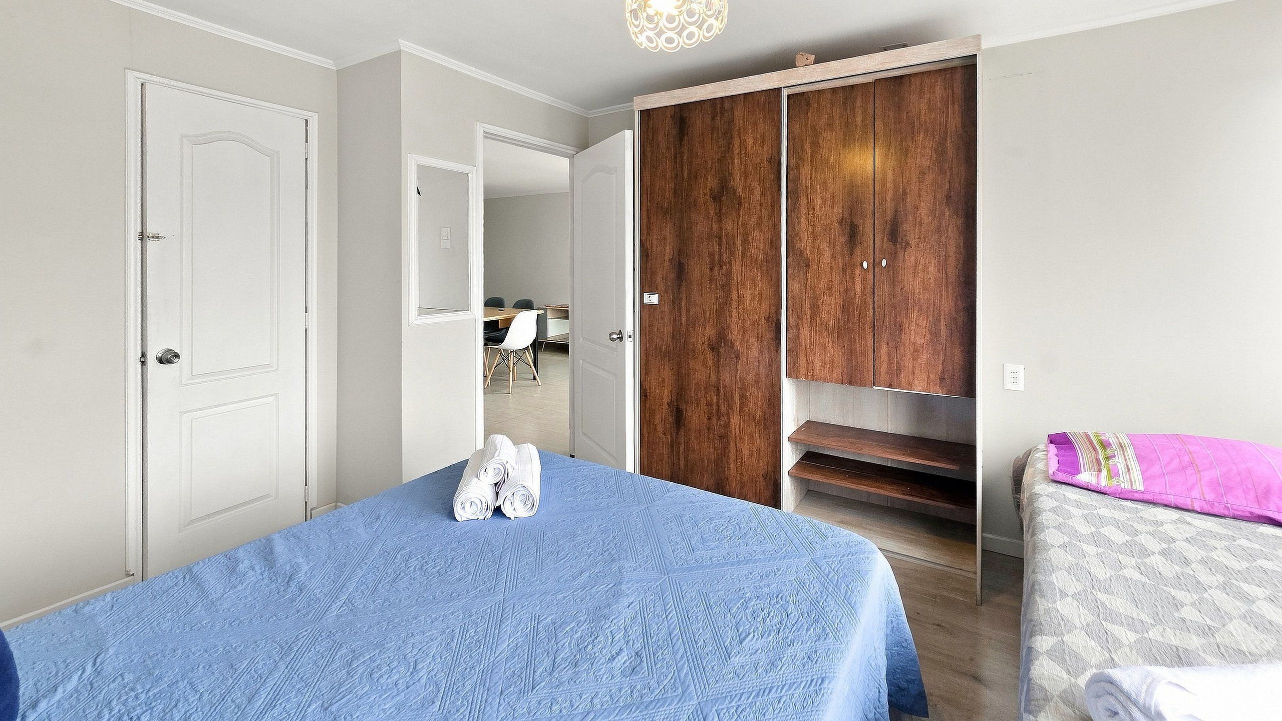 A bedroom with a bed, a wardrobe, and a desk with chairs.