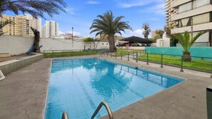 A swimming pool with a metal ladder, surrounded by a low wall and palm trees.