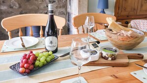 Una mesa de comedor dispuesta con una botella de vino, una copa, un plato de uvas, queso y pan.