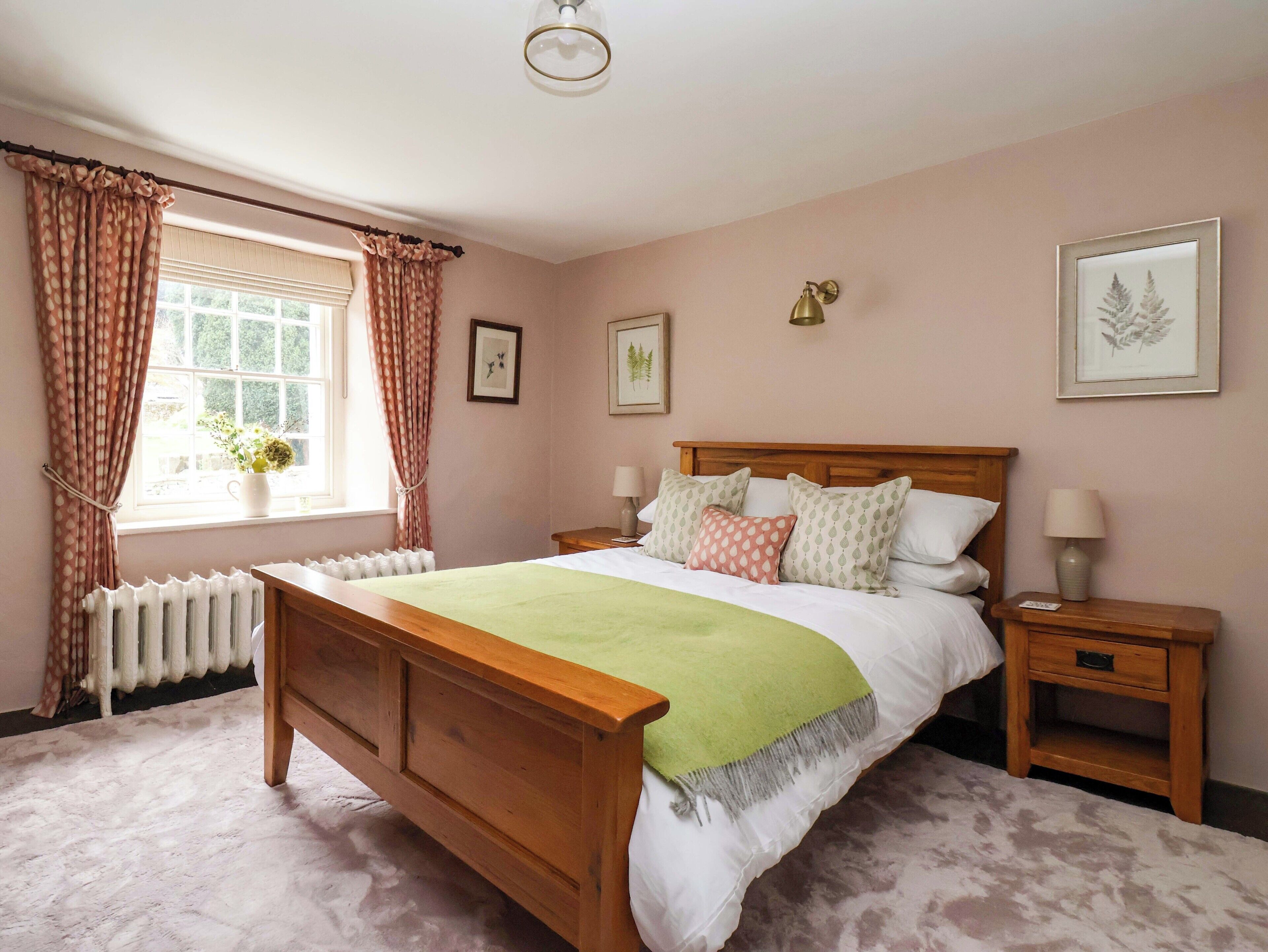 A bedroom with a wooden bed, a nightstand, a radiator, and a window with curtains.