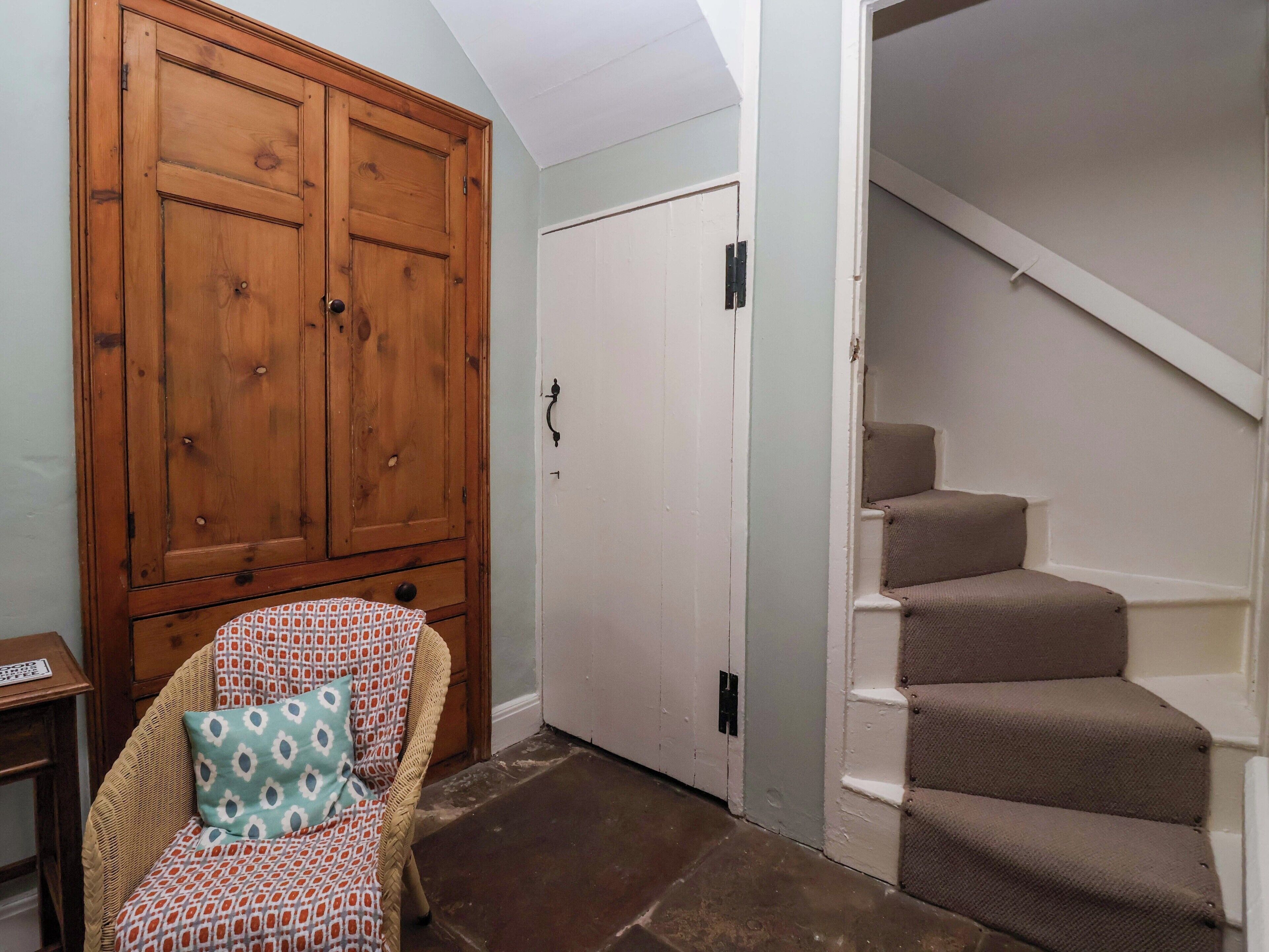 A room with a wooden wardrobe, a chair with a patterned cushion, a white door, and a staircase with beige steps.