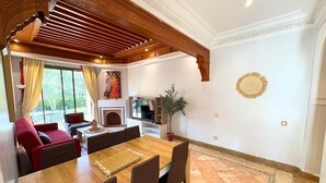 A dining area with a wooden table and chairs, a fireplace, and a TV. - appartement piscine la palmeraie  (Marrakech)