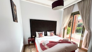 A hotel room with a large bed, a nightstand, a ceiling light, and a view of the outdoors. - appartement piscine la palmeraie  (Marrakech)