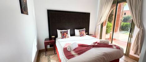 A hotel room with a large bed, a nightstand, a ceiling light, and a view of the outdoors.