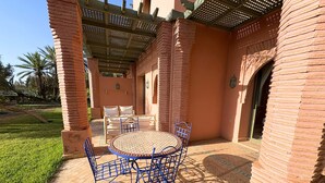 A patio with a round table and blue chairs, surrounded by brick walls and a pergola. - appartement piscine la palmeraie  (Marrakech)