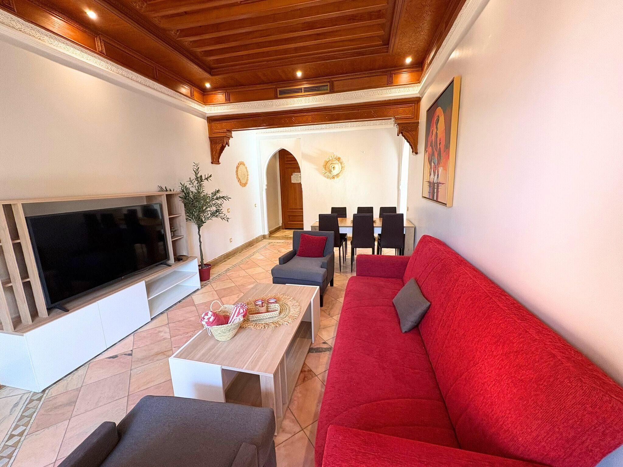 Un salon doté d’un grand téléviseur à écran plat, d’un canapé rouge, d’un canapé gris et d’une table basse en bois agrémentée d’objets décoratifs.