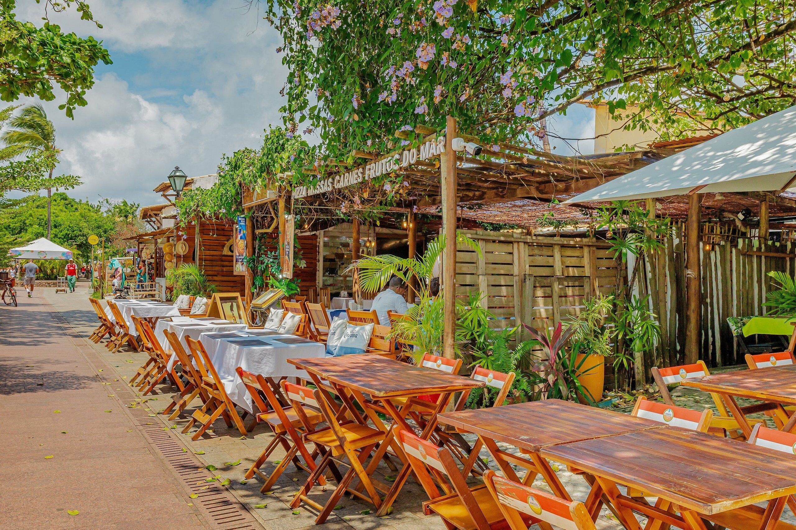 Un restaurant en plein air avec des tables et des chaises en bois, entouré de verdure et agrémenté d’une pergola en bois.
