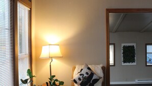A cozy living room with a brown leather sofa, a white fluffy throw, and a panda-themed pillow. A lamp provides soft lighting, and a large mirror reflects the room. - Kelso Pitstop (Kelso)