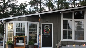 A house with a dark exterior, white-framed windows, a black front door, and a welcome sign. There are potted plants and a bench outside. - Kelso Pitstop (Kelso)