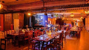 Un restaurante con varias mesas, un escenario con instrumentos musicales y un ambiente cálido, iluminado con tonos anaranjados.