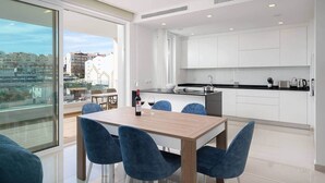 A modern apartment with a dining area, kitchen, and large windows offering a city view.