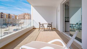 A balcony with a table and chairs, a glass door, and a view of buildings in the background.