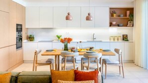 Une cuisine moderne avec des meubles blancs, une table à manger pour quatre personnes et des luminaires suspendus au-dessus.