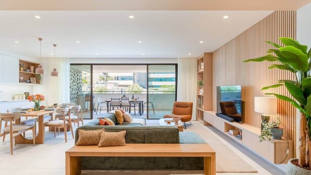 Un salon moderne avec un canapé, une table basse et un téléviseur. Il y a également un coin repas avec des chaises et une table. La pièce est dotée de grandes fenêtres et d’un balcon.