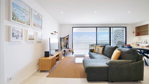 A modern living room with a large window, a grey sofa, and a wooden cabinet.