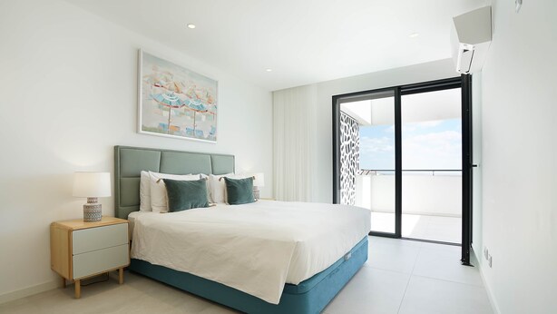 A modern bedroom with a bed, a nightstand, a painting, and a view through a glass door.