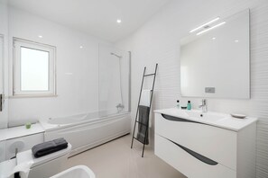 Ein modernes Badezimmer mit einer Badewanne, einem großen Spiegel und einem Waschtisch.