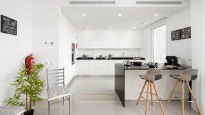 A modern kitchen with white cabinets, a central island, and two bar stools. - CourtView Modern Lagos Apartment (Lagos)