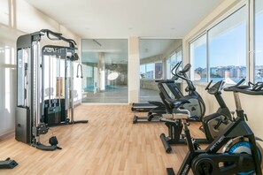 Ein modernes Fitnessstudio mit Cardiogeräten, Krafttrainingsgeräten und großen Fenstern mit Blick auf die Stadt.