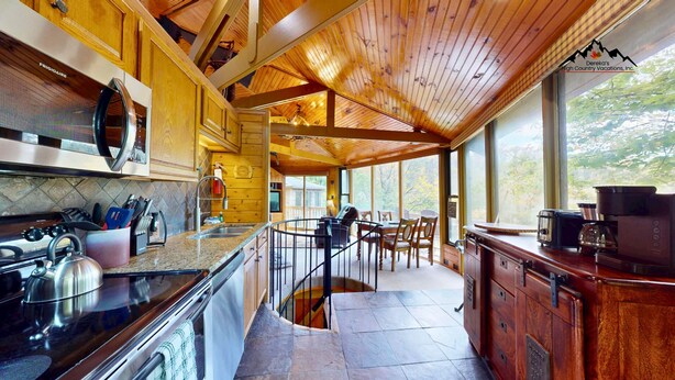 A kitchen with granite countertops, a stove, and a sink. There is a dining area with a table and chairs.