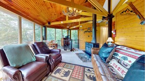 A cozy cabin interior with leather sofas, a fireplace, and a large window offering a view of the outdoors.