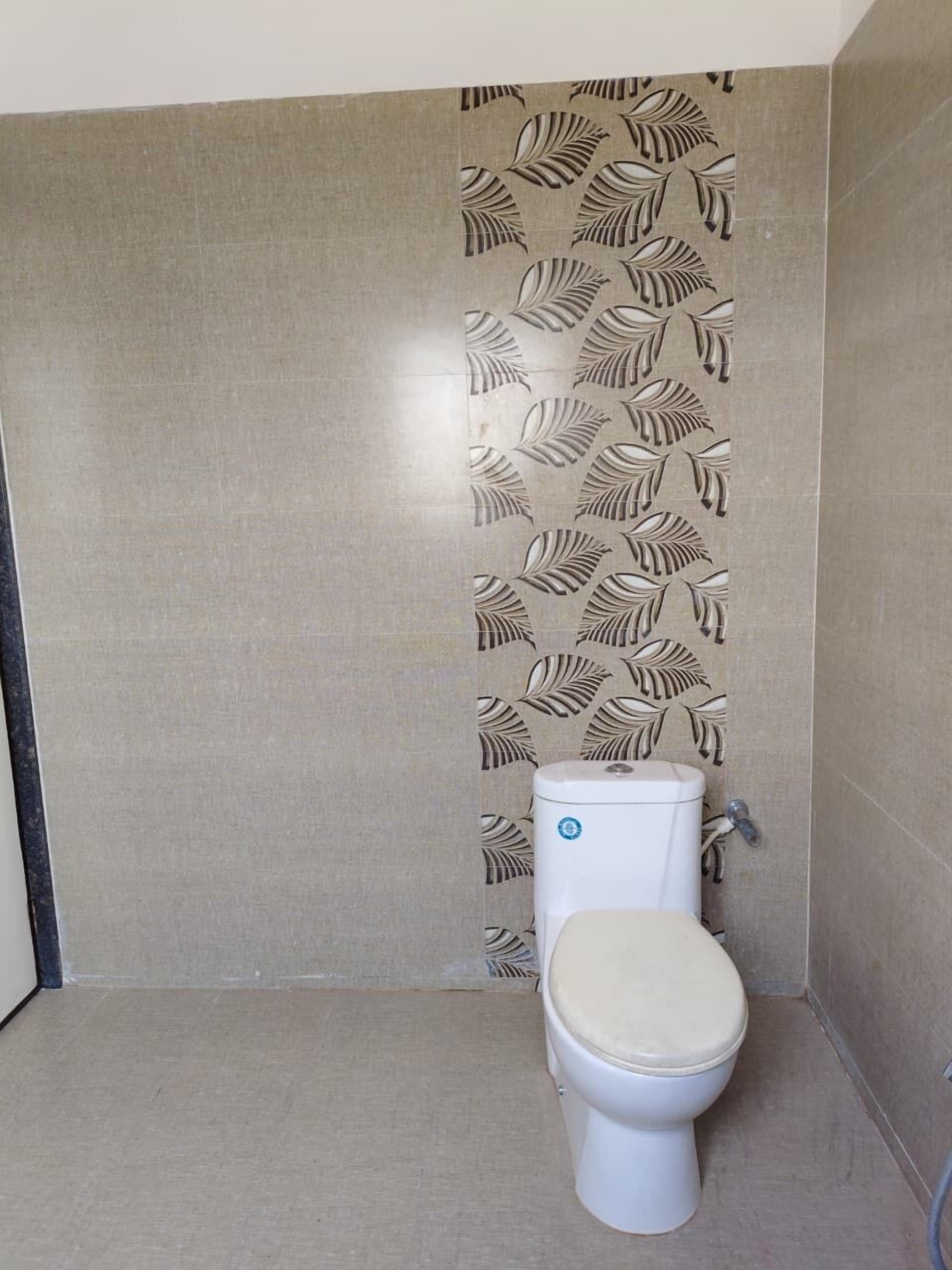 Un baño pequeño y moderno con un inodoro, una pared con diseño de hojas y un piso sencillo.
