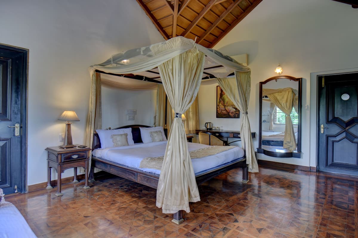 A four-poster canopy bed with a wooden headboard, a bedside table with a lamp, and a large mirror on the wall.