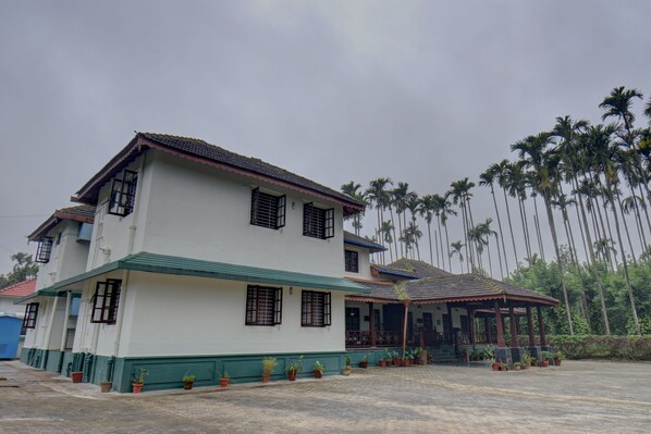 A two-story building with a balcony, surrounded by potted plants and palm trees. - Siddhanta manor (Sakleshpur)