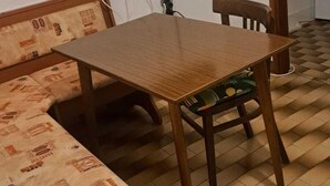 Una habitación con una mesa de madera, dos sillas, un sofá y un televisor montado en la pared.