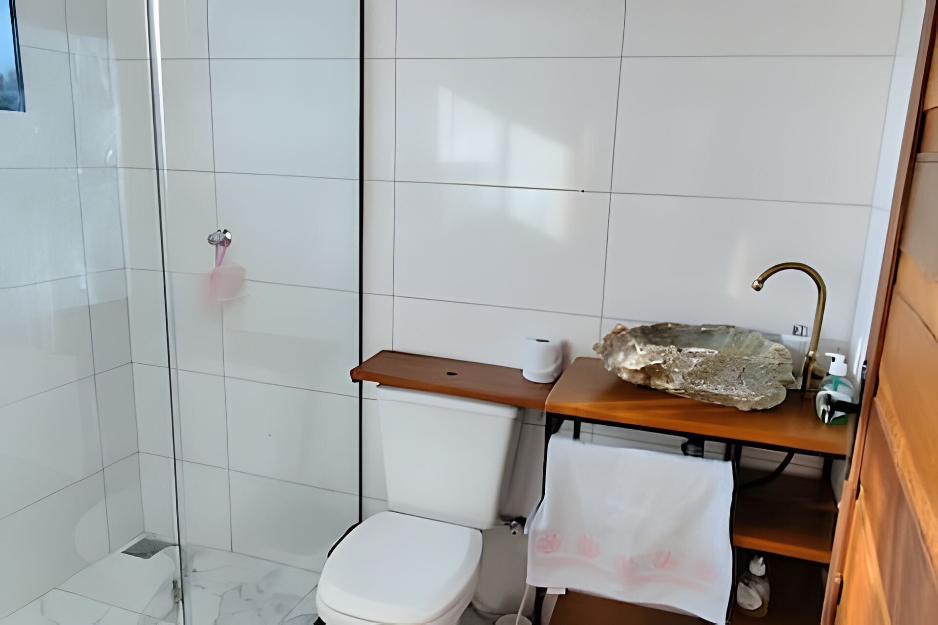 A bathroom with white tiles, a toilet, a sink with a stone basin, and a towel hanging on a shelf.