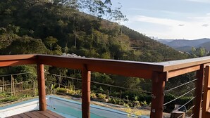 A wooden deck overlooking a pool with a view of a forested hillside and distant mountains. - Oceana Suites Ponto Alto (Domingos Martins)