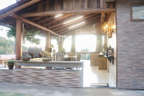 Een overdekt terras met houten balken, plantenpotten en een moderne bar.