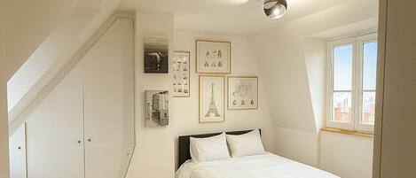 A bedroom with a bed, a checkered rug, and framed pictures on the wall.