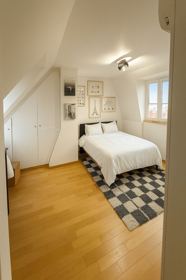 A bedroom with a bed, a checkered rug, and framed pictures on the wall.