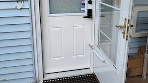 Une porte d’entrée blanche avec un panneau de verre, un paillasson sur lequel est écrit « BIENVENUE », et une boîte aux lettres sur le côté droit.