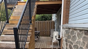 Une terrasse en bois avec un muret en pierre, un espace abrité et une table entourée de chaises.
