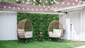 A patio with two wicker chairs, a small table, and a lush green wall.
