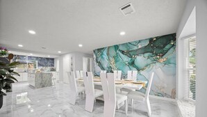 A modern dining area with a marble floor, white chairs, and a large wall mural.