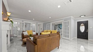 A spacious living room with a large brown leather sofa, a fireplace, and a black door with a decorative glass window.