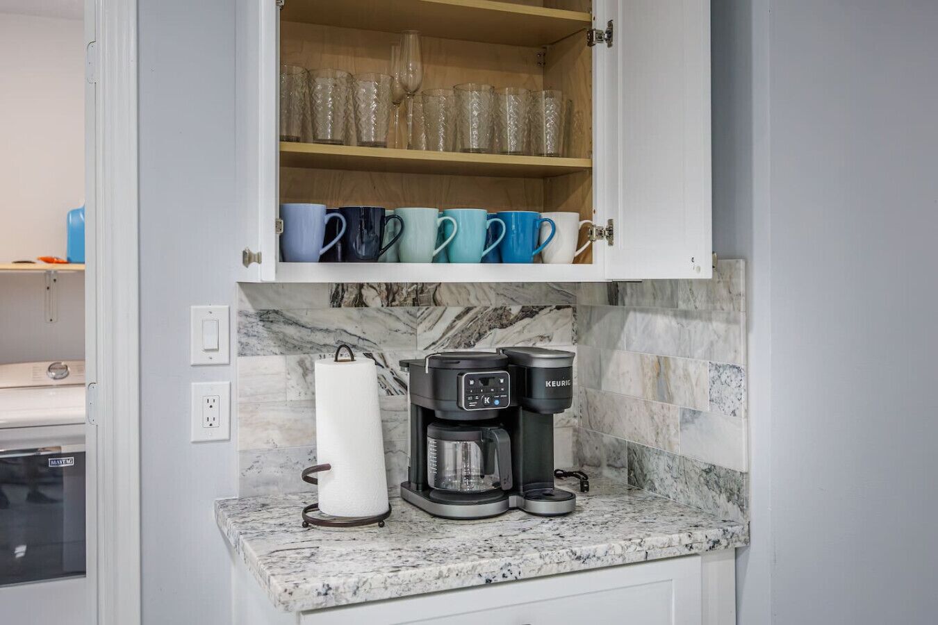 Een keuken met een koffiezetapparaat, een houdertje voor keukenpapier en een bekerrek.